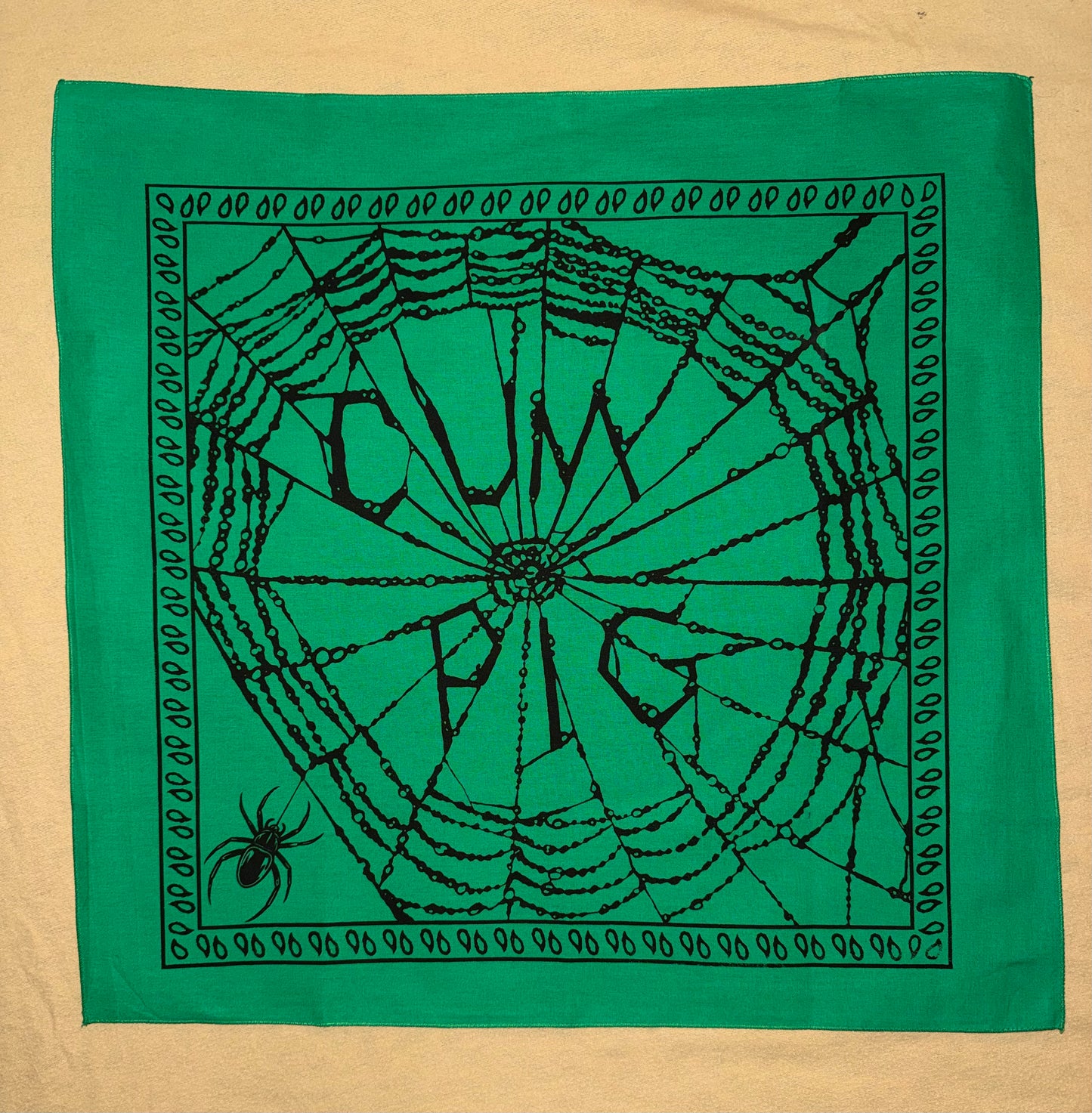 Hand-silk-screened cotton bandana featuring a spiderweb typography graphic printed in black ink on green fabric.