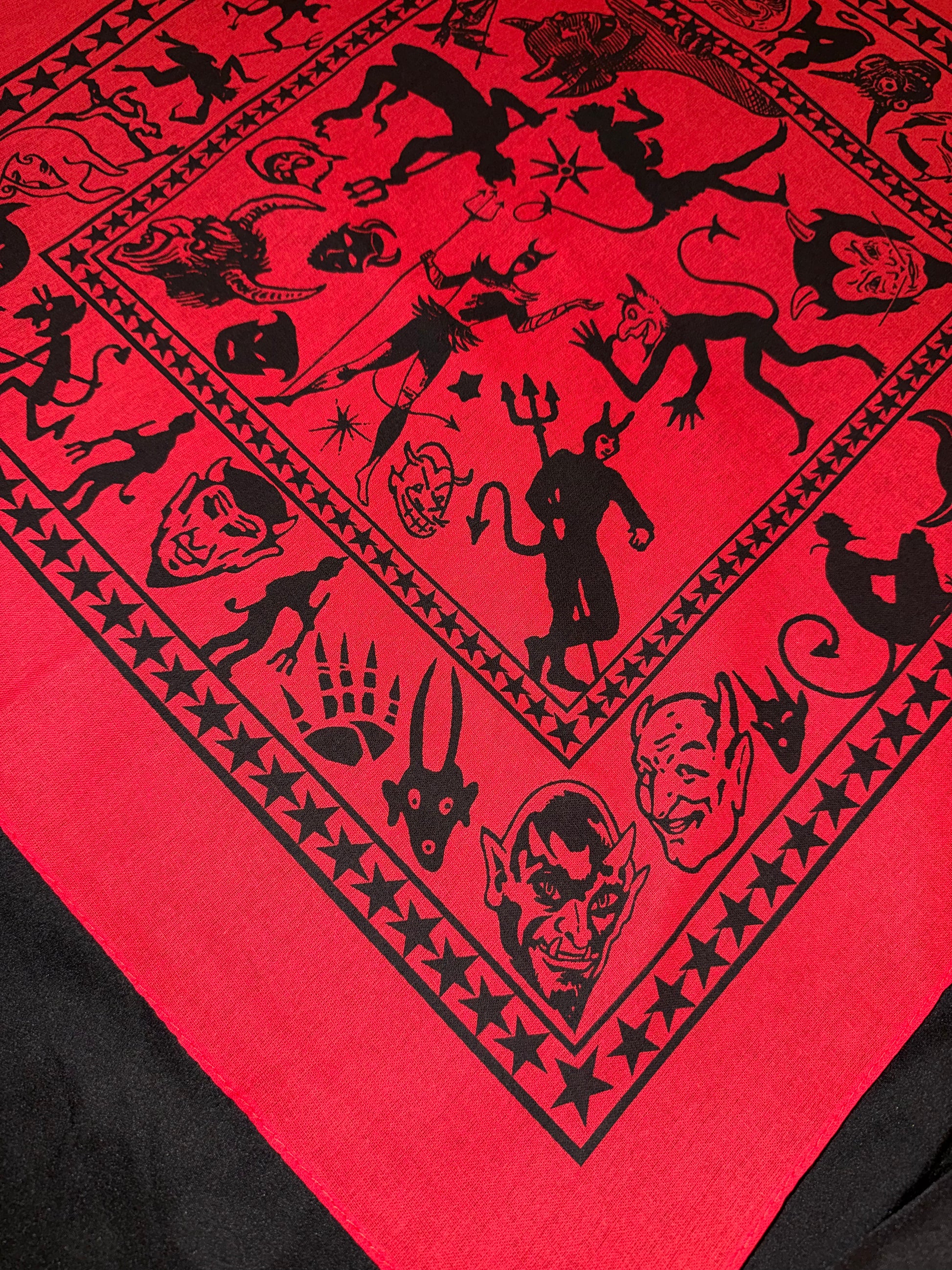 Close-up detail of a hand-silk-screened cotton bandana featuring vintage-style devil illustrations printed in black ink on red fabric.
